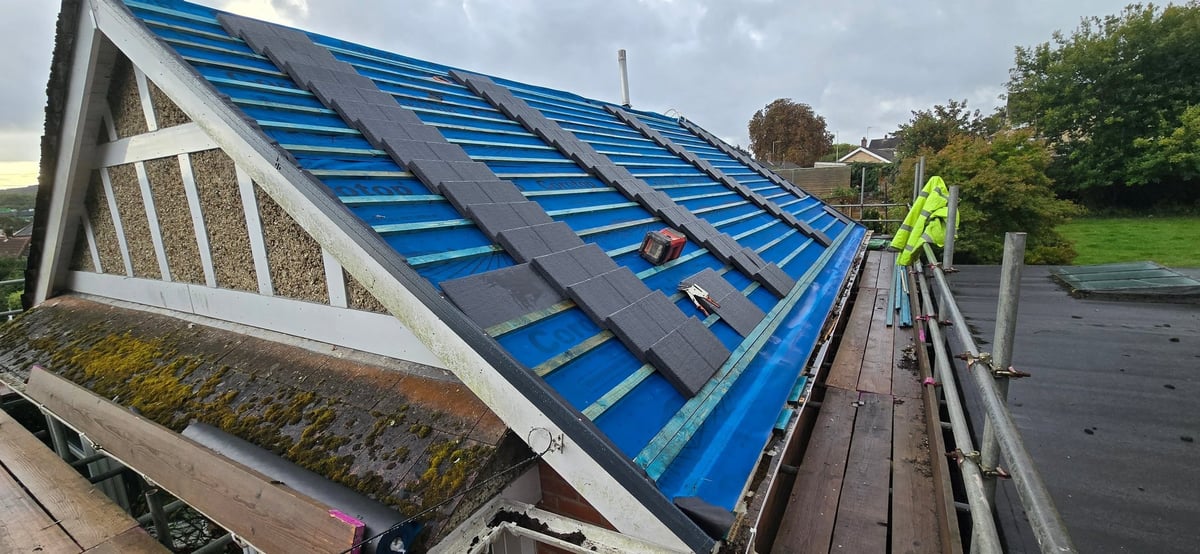 Worker installing blue metal roofing panels on a residential roof under construction