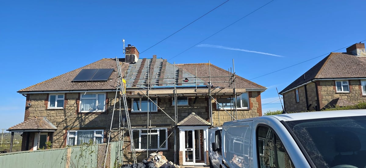 Brick house under renovation with scaffolding, white van parked in front, clear blue sky