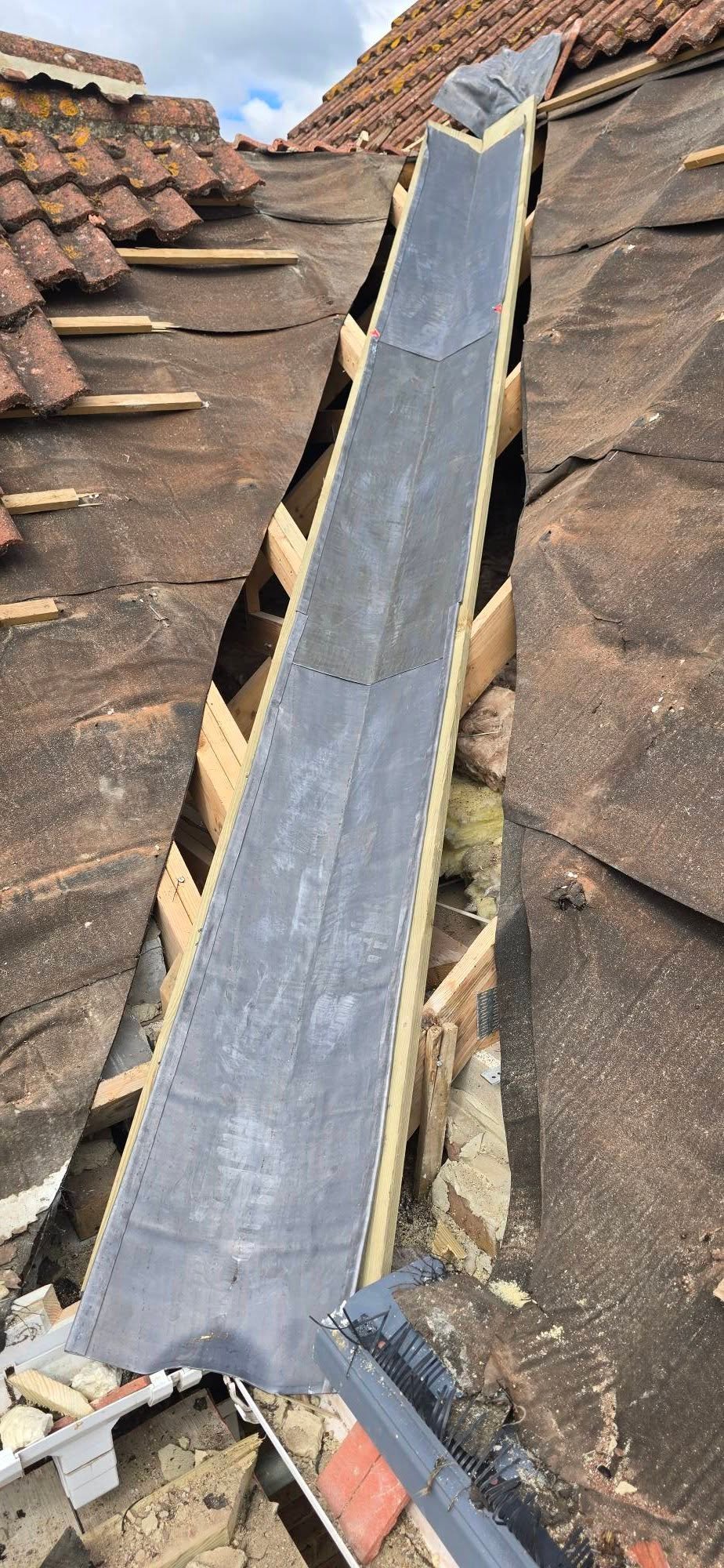 Roof gutter installation with dark metal downspout between aged terracotta tiles on a residential building